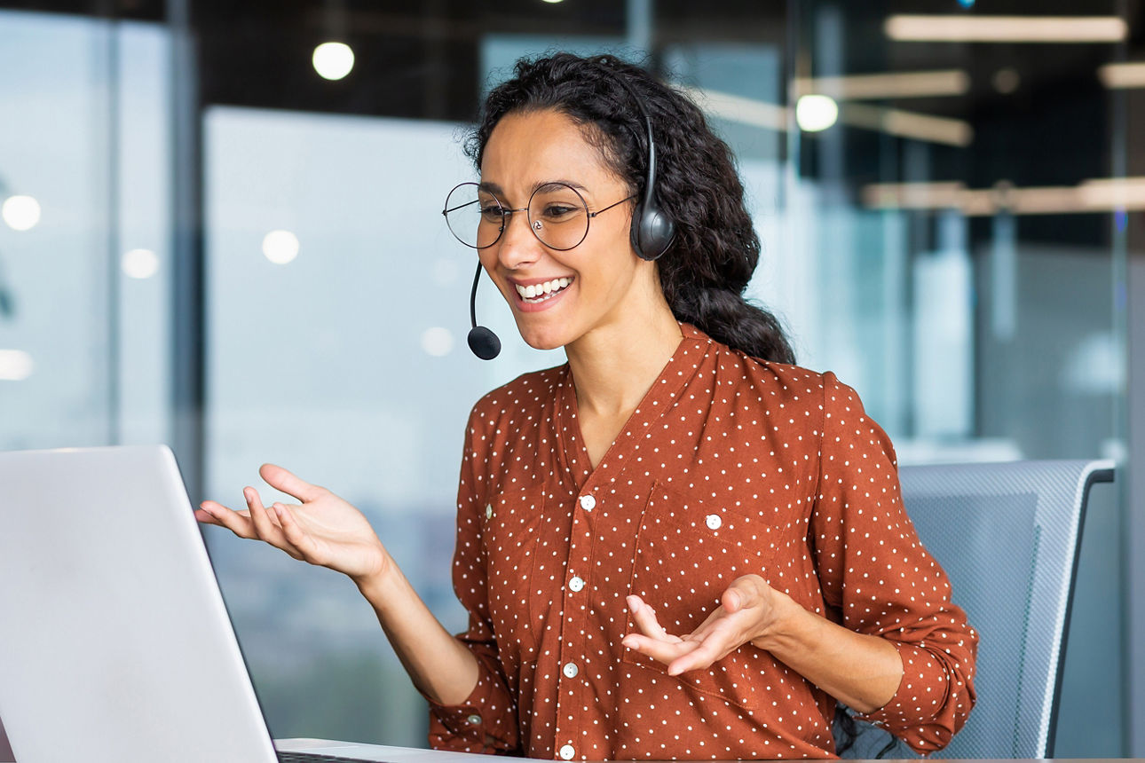 Eine Frau mit dunklen Haare führt ein Telefongespräch über ein Headset an einem Laptop
