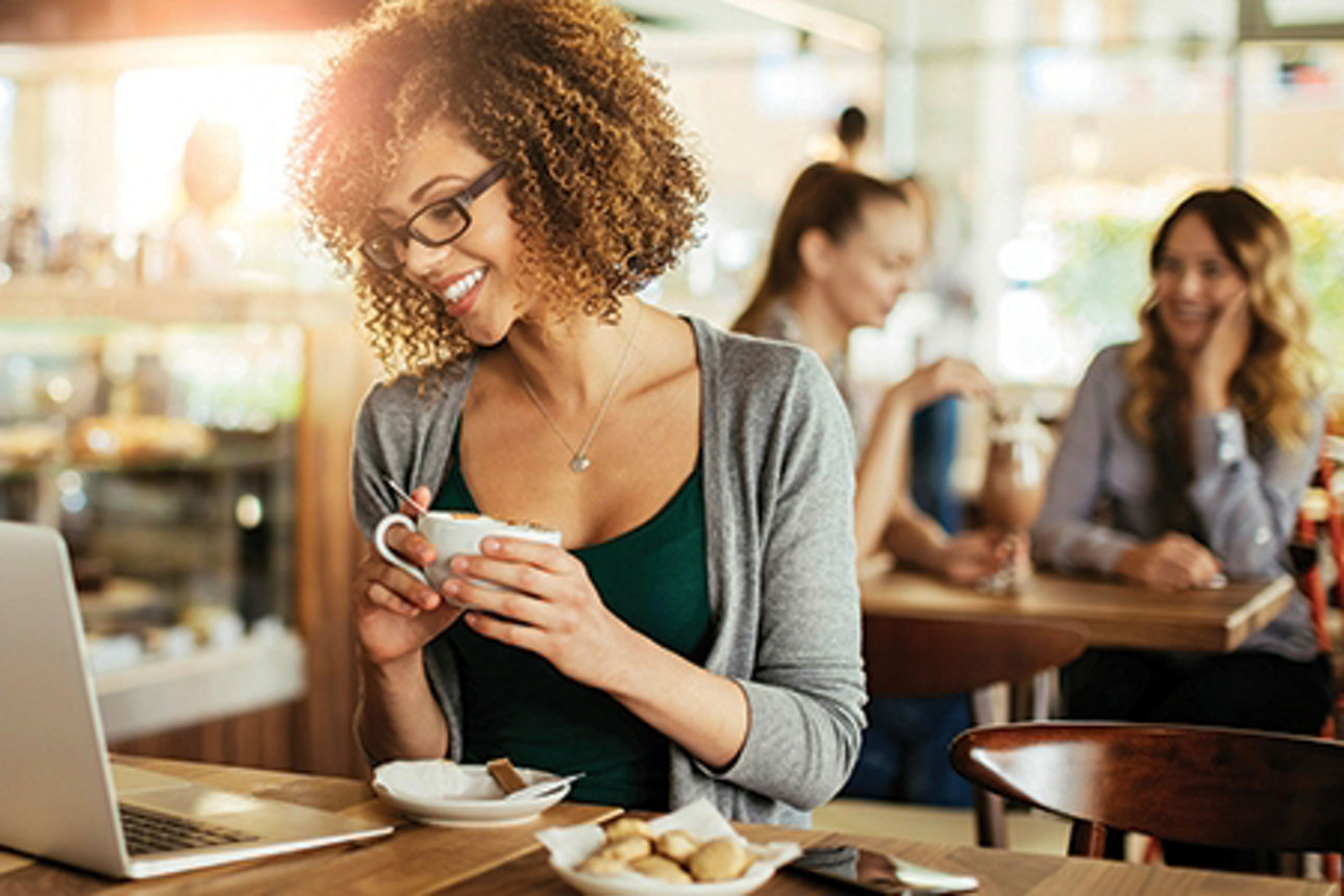 Webkonferenzen: junge Frau sitzt in einem Café mt ihrem Laptop