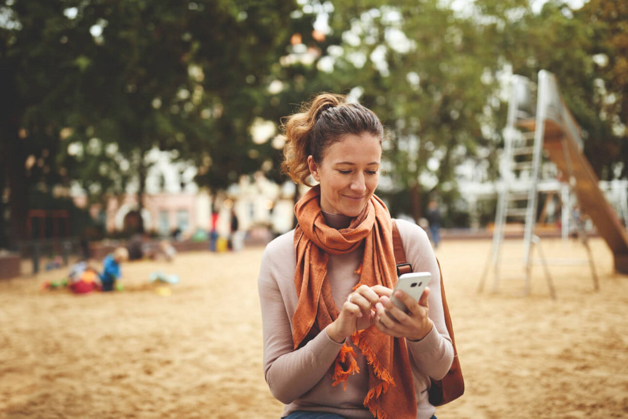 Junge Frau auf einem Spielpaltz mit ihrem Handy.