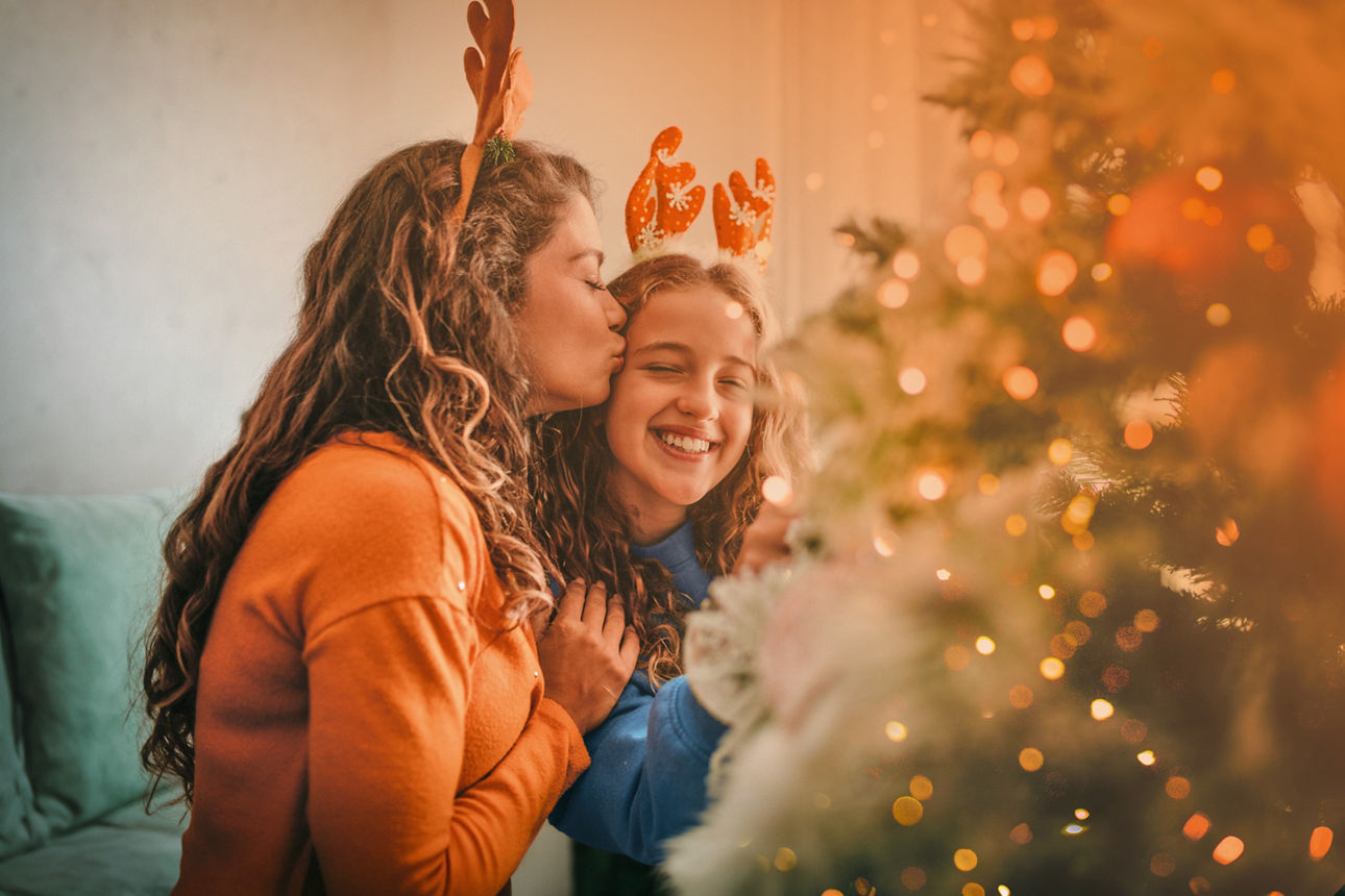 Frau küsst Tochter auf die Stirn. Der Raum ist weihnachtlich geschmückt.