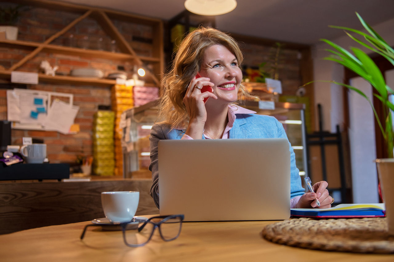 Frau im Café sitzt vor dem Laptop und telefoniert