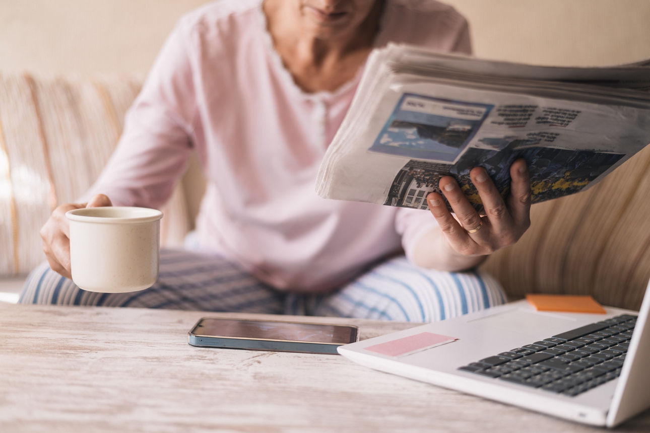 Frau auf dem Sofa mit einer Tasse Kaffee liest Zeitung.
