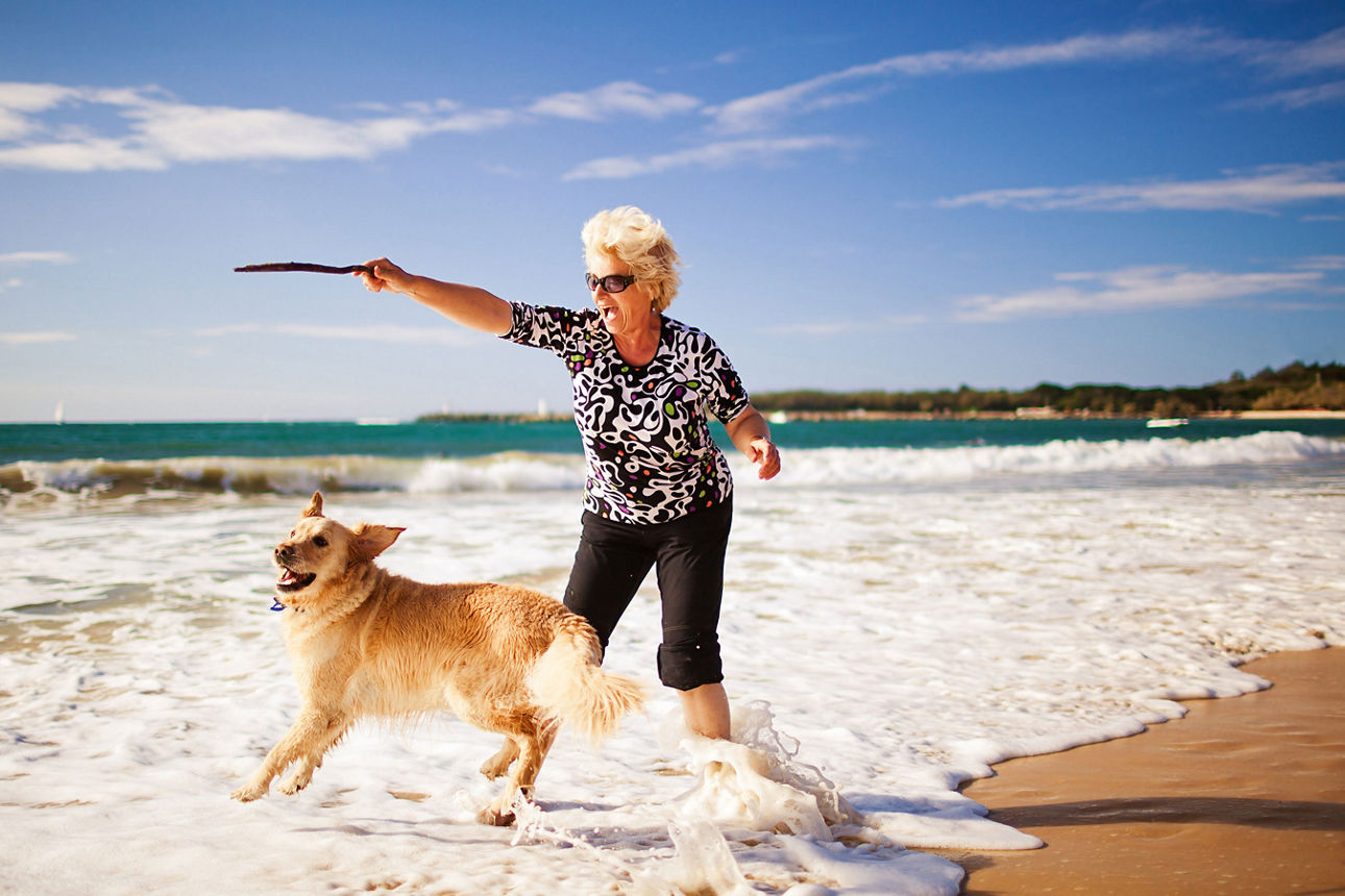 Blonde Frau spielt mit Hund am Strand