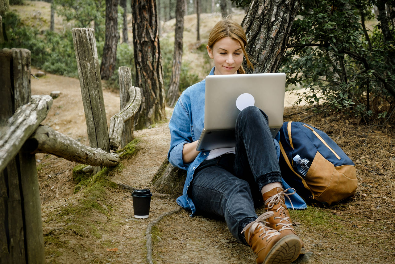 Eine Frau in der Natur sitzend mit Laptop in der Hand