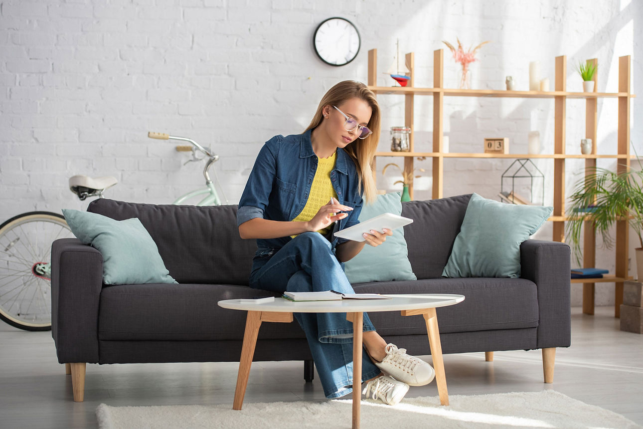 Frau sitzt mit einem Tablet auf einem Sofa
