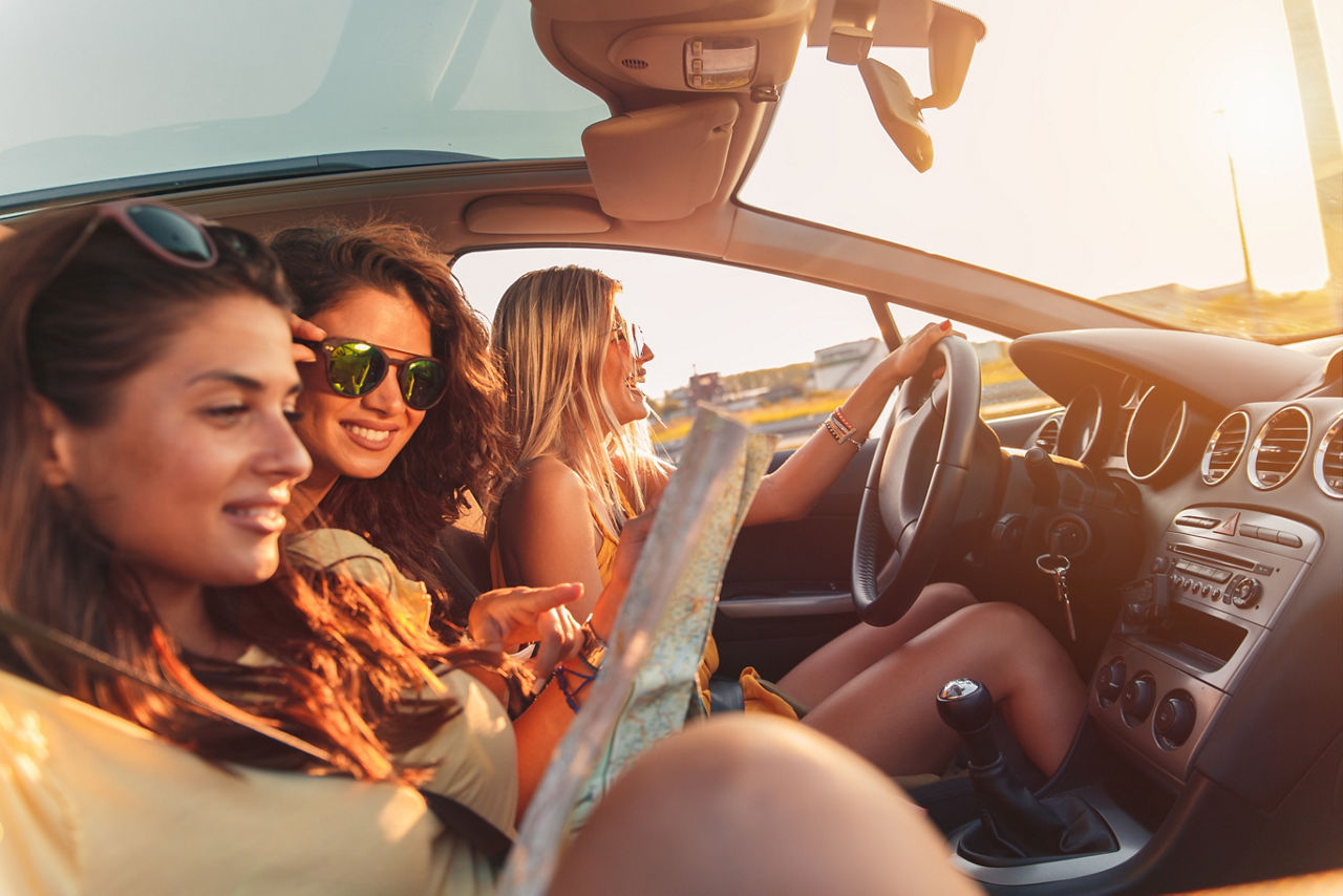 Drei Frauen im Auto.Eine Frau trägt Sonnenbrielle und eine Frau hält einen Stadtplan.