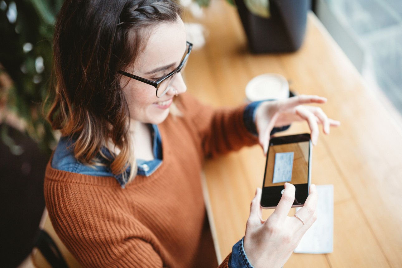 Eine lächelnde junge Frau fotografiert mit ihrem Smartphone einen Scheck zur Überweisung