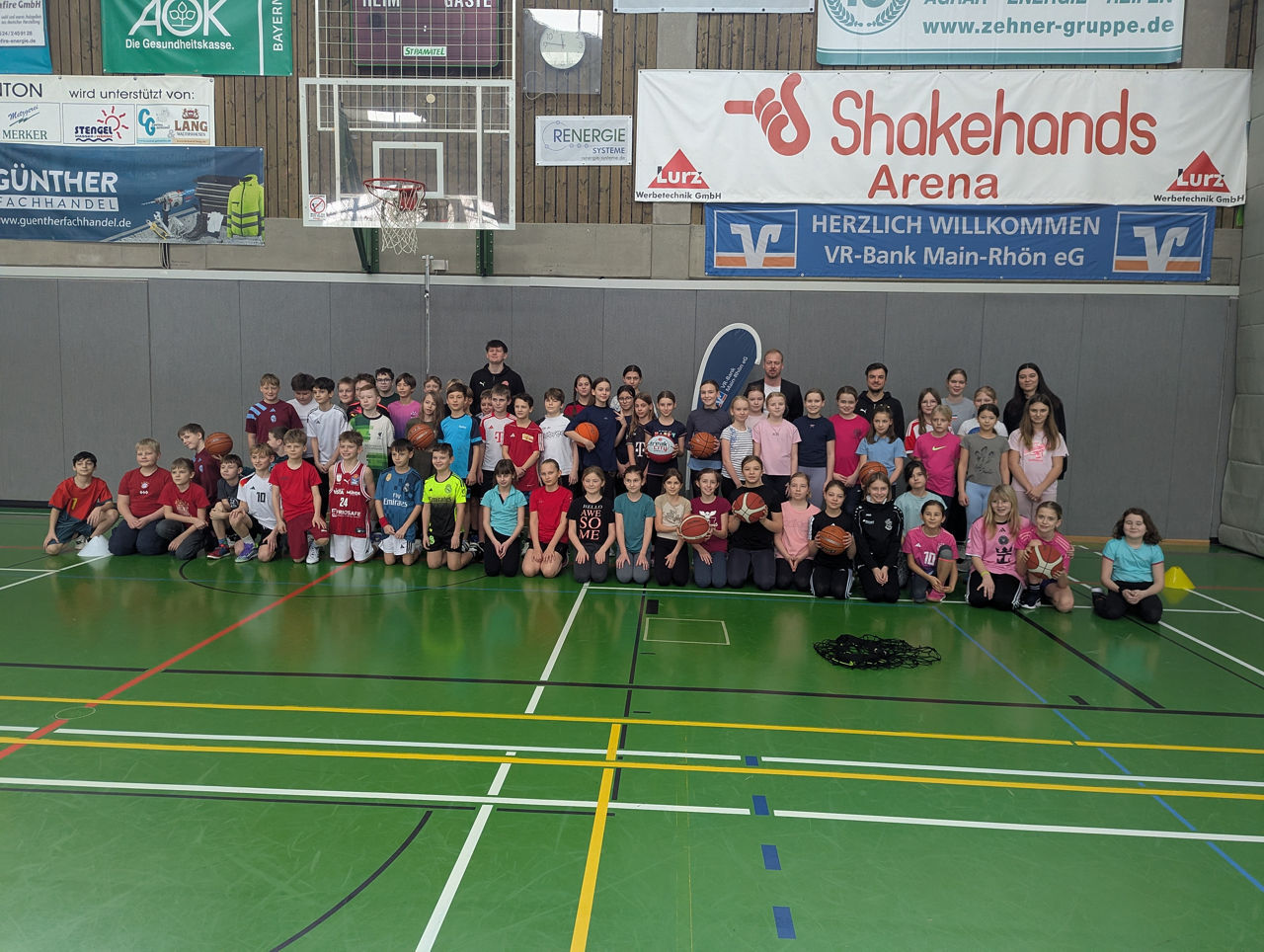 Zu sehen ist das das Jugendtrainerteam des Freak City Bamberg e.V. mit Schülerinnen und Schülern der fünften Jahrgangsstufe der Dr.-Karl-Grünewald-Realschule. Das Foto wurde in einer Turnhalle gemacht.