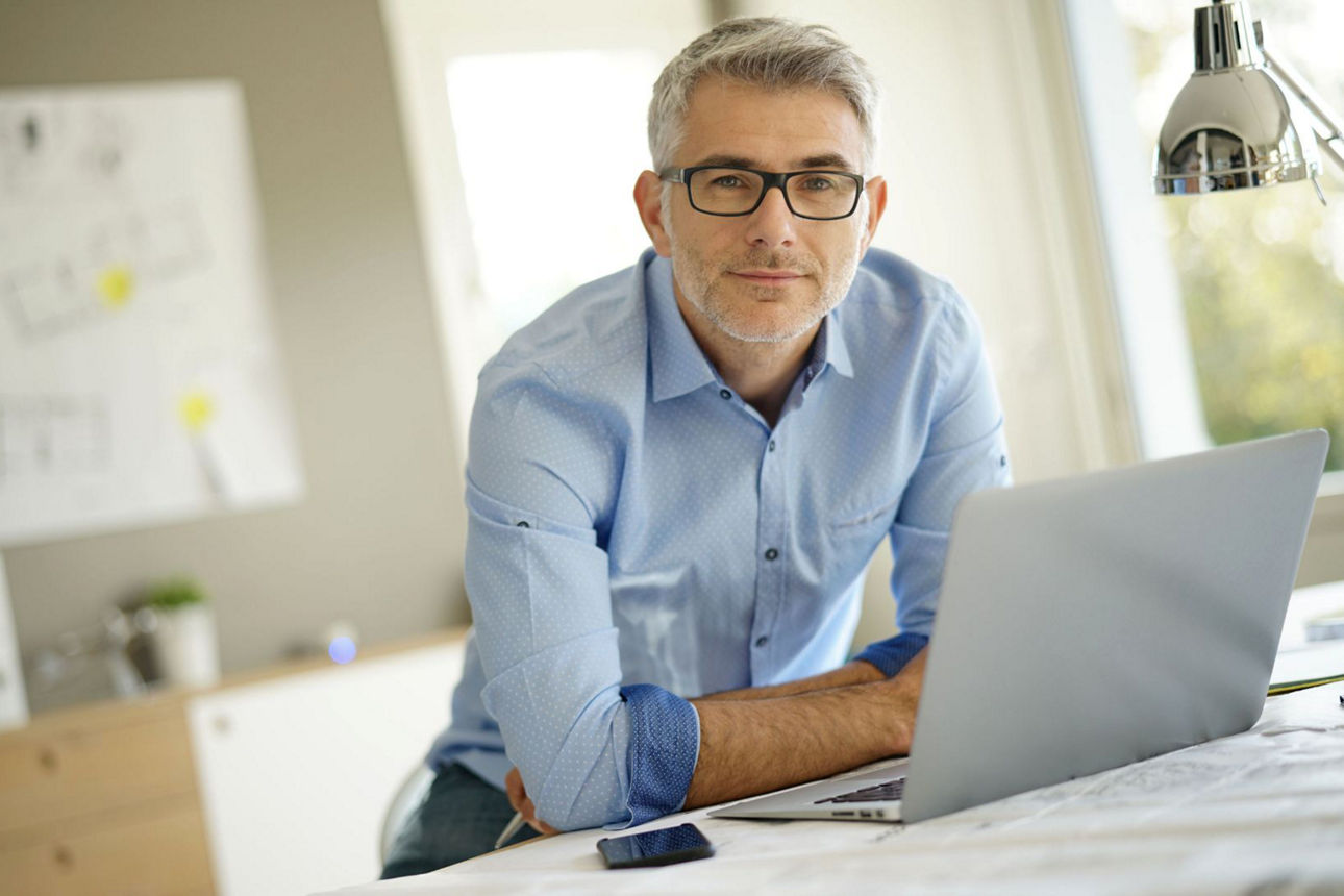 Ein Mann stützt seine Ellenbogen auf einem Tisch ab und schaut über einen Laptop