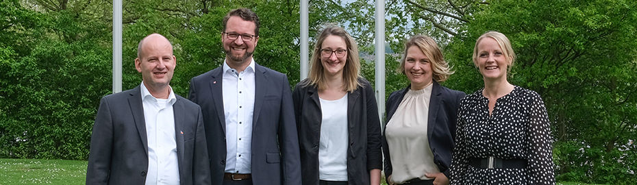 Eine Gruppe von fünf Beratern und Beraterinnen steht draußen und lächelt in die Kamera
