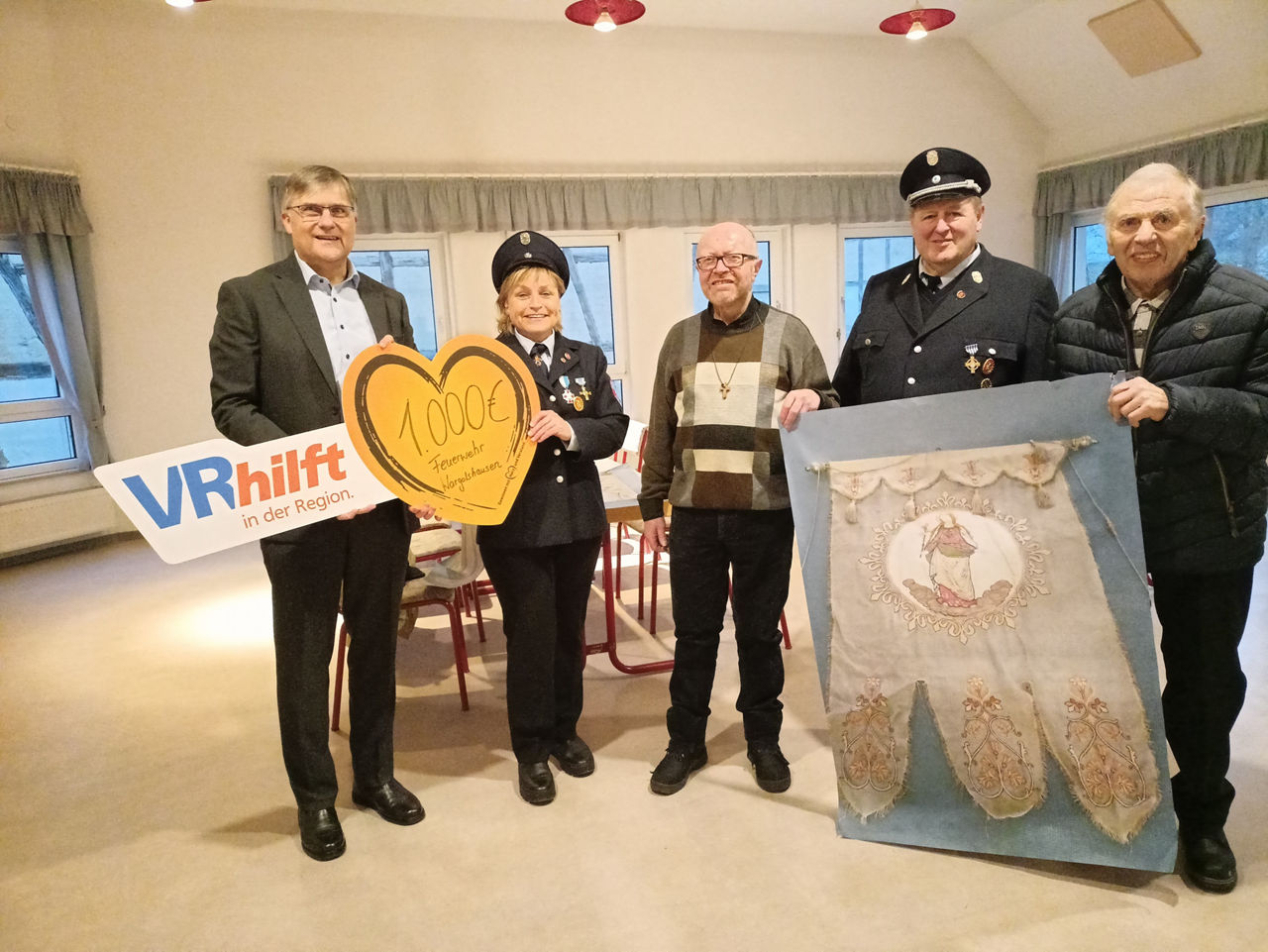 Das Bild zeigt vier männliche Personen und eine Frau in einem Raum. Sie halten ein herzförmiges Schild mit der Aufschrift "1.