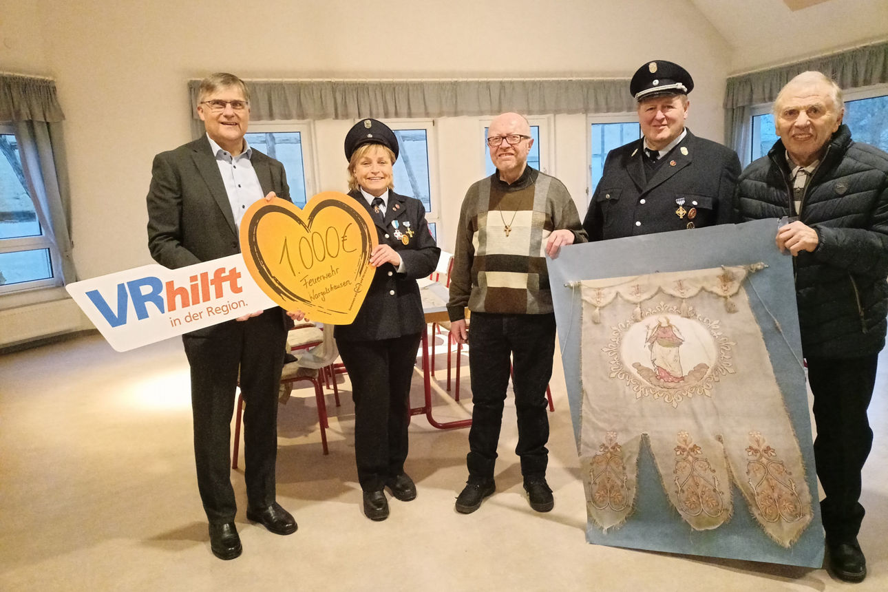 Das Bild zeigt vier männliche Personen und eine Frau in einem Raum. Sie halten ein herzförmiges Schild mit der Aufschrift "1.