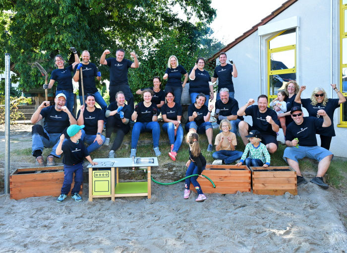 Eine Gruppe von Menschen jubeln nach getaner Arbeit am Außengelände eines Kindergartens