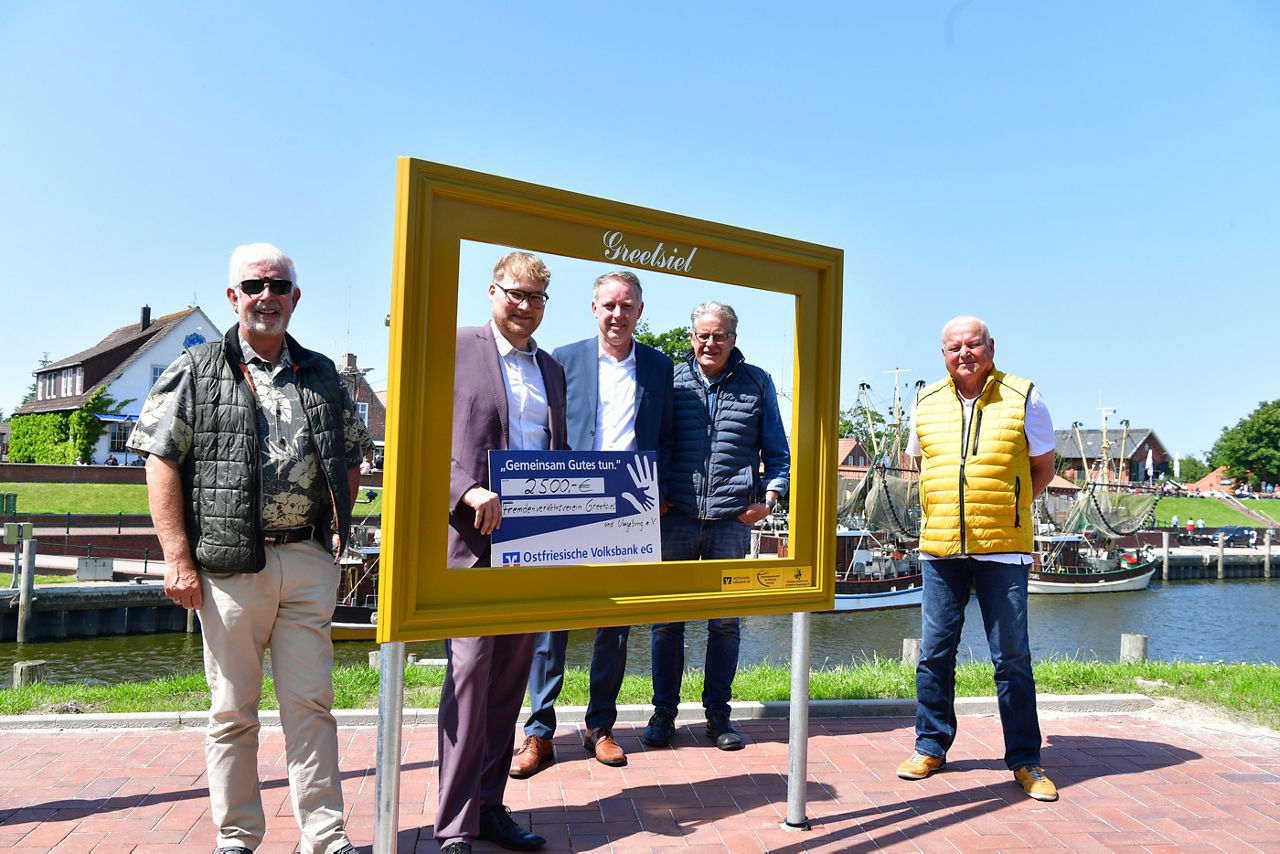 Mitglieder des Fremdenverkehrsvereins und Mitarbeiter der Volksbank bei der Scheckübergabe vor dem neuen Bilderahmen am Hafen