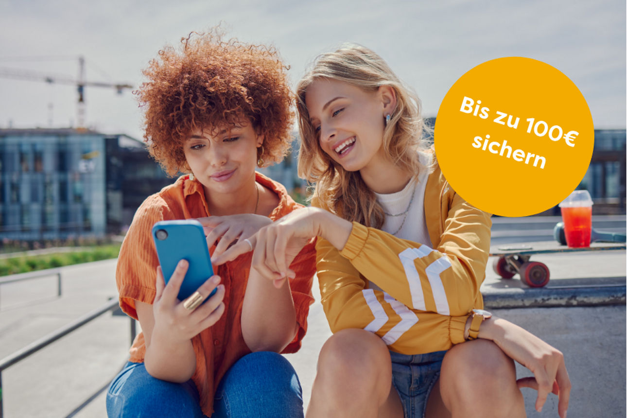 Zwei Frauen sitzen auf einer Bank und schauen auf ihr Handy.