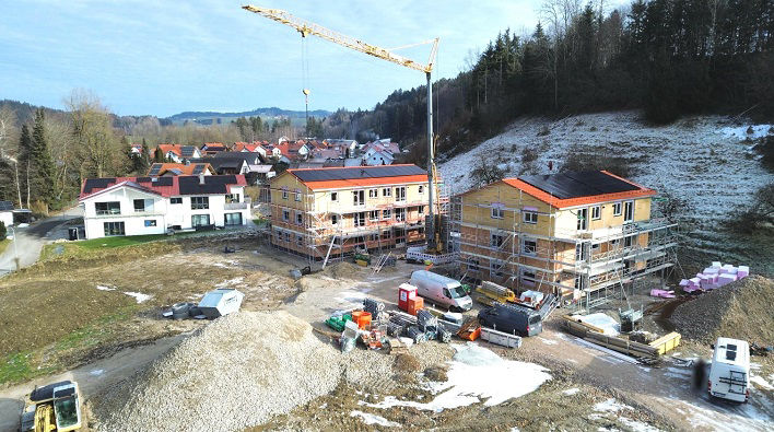 Zwei Häuser in winterlicher Landschaft werden gebaut. Es sind Baustellenfahrzeuge zu sehen. Ein großer Krank steht in der Mitte.