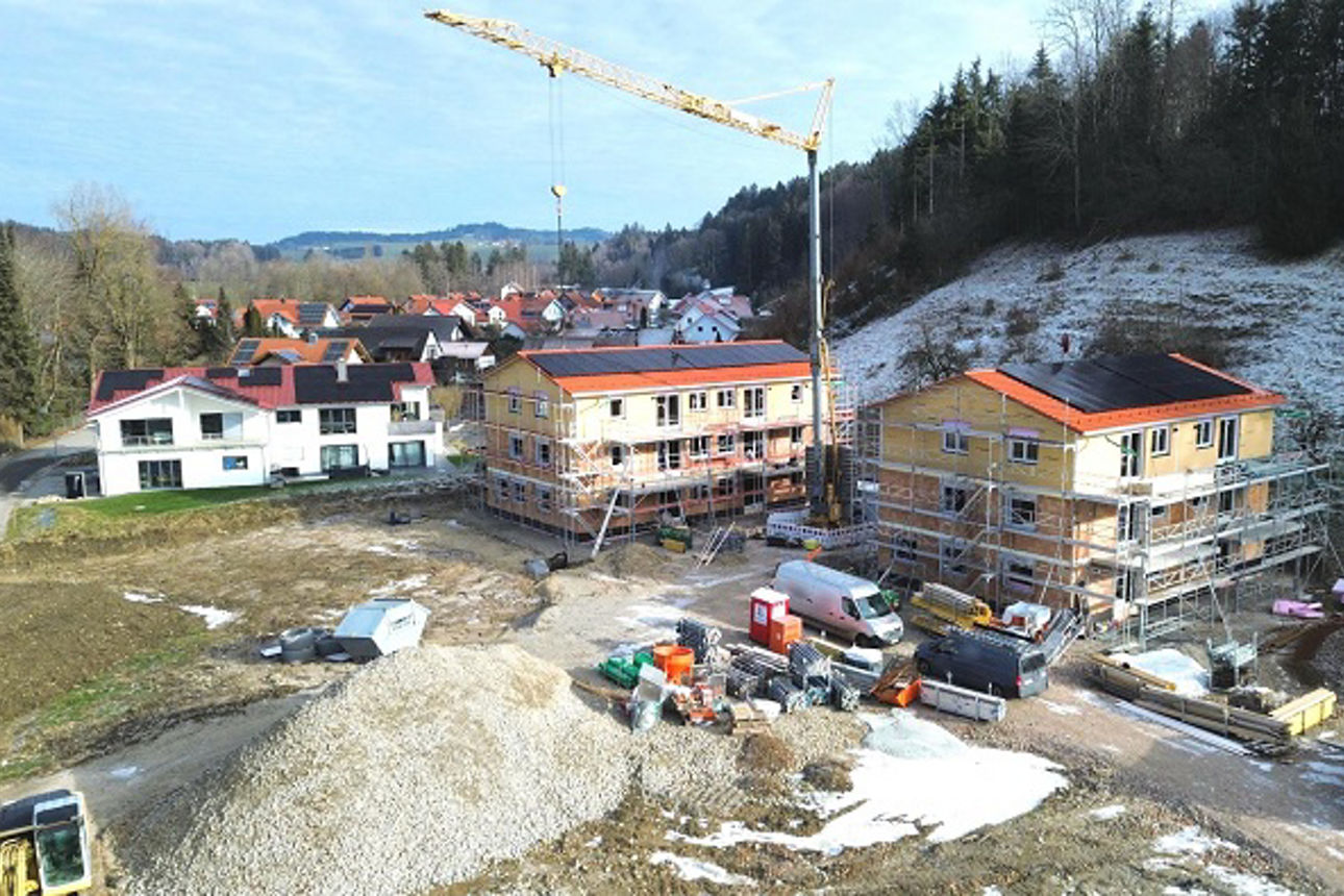 Zwei Häuser in winterlicher Landschaft werden gebaut. Es sind Baustellenfahrzeuge zu sehen. Ein großer Krank steht in der Mitte.