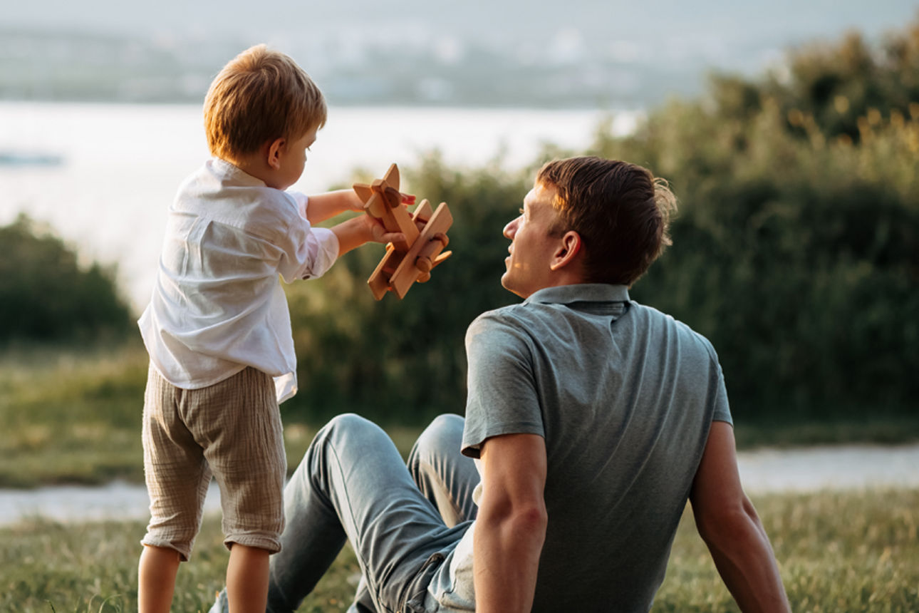 Vater mit Sohn der ein Modellflugzeug in der Hand hat auf einer Wiese