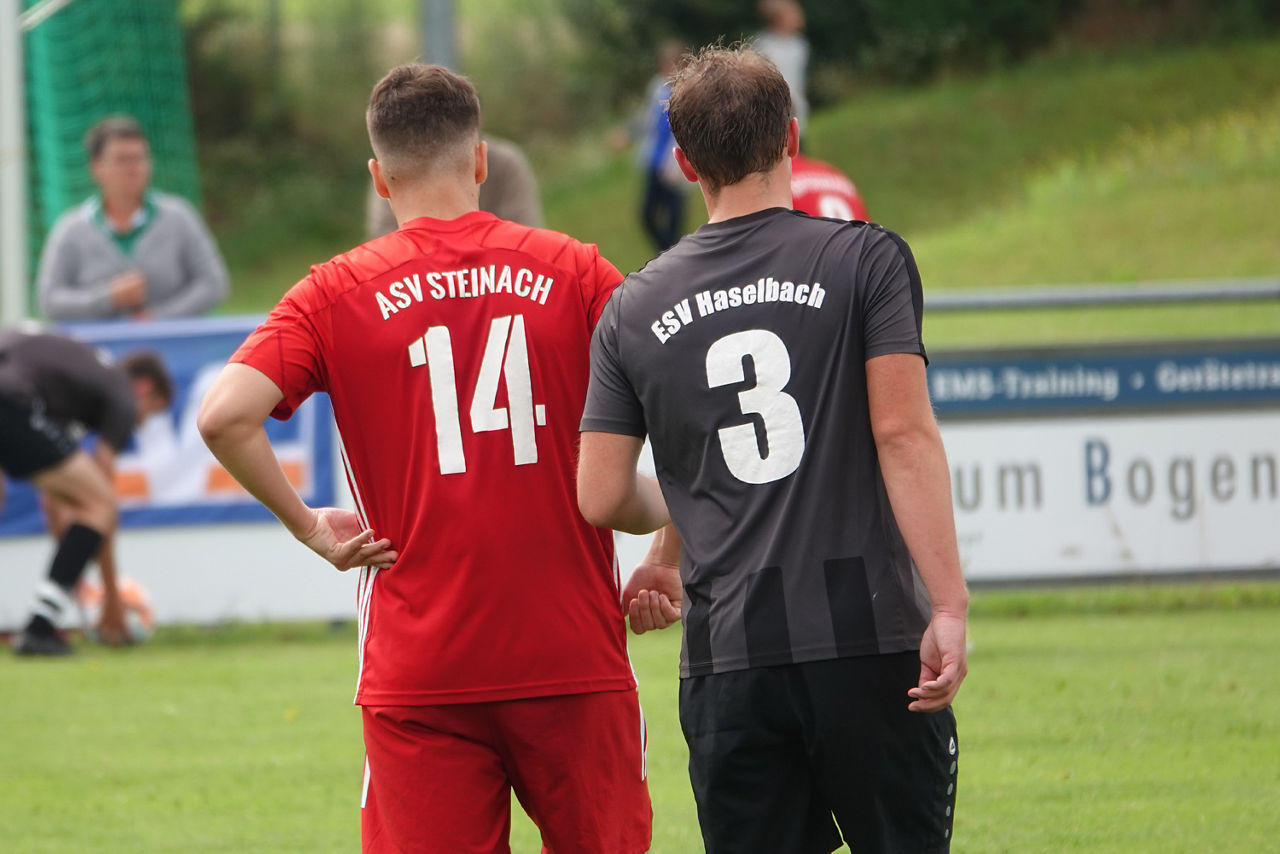 Zwei Fußballspieler aus unterschiedlichen Teams laufen auf dem Spielfeld.