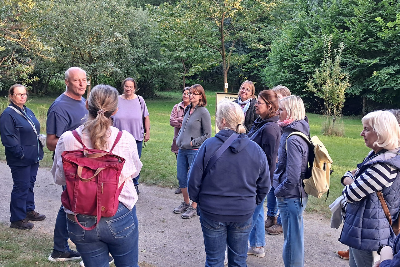 Auf einem Weg im Grünen stehen die Teilnehmerinnen der Kräuterwanderung zu einer Erklärung von Werner Gahlen in lockerer Runde zusammen.