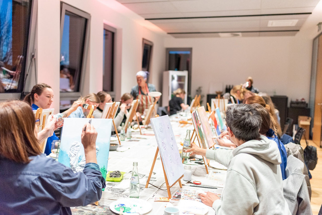 Frauen mal auf einer kleinen Staffelei zusammen an einem langen Tisch