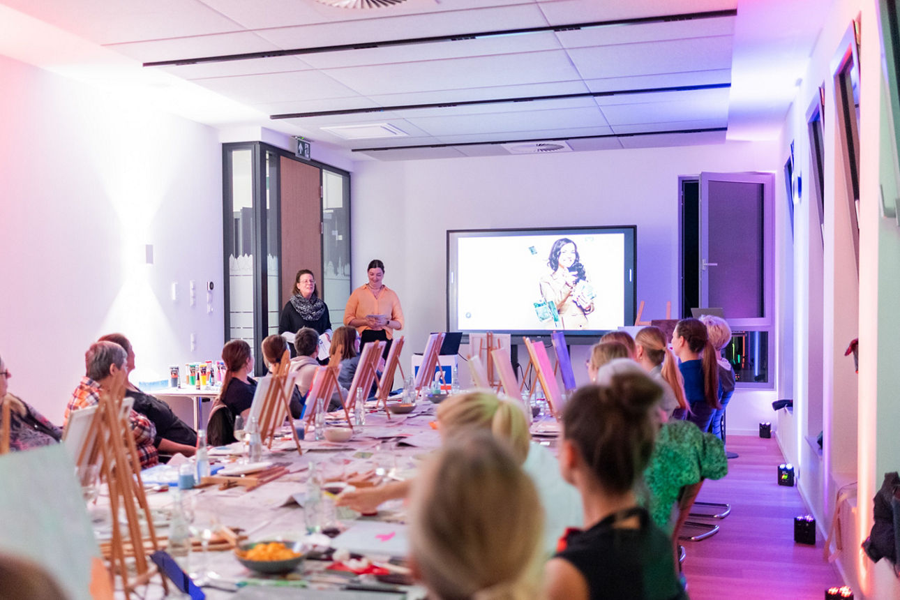 Frauen und Finanzen Abend: Frauen sitzen an einem langen Tisch und malen - zwei Mitarbeiterinnen halten Vortrag