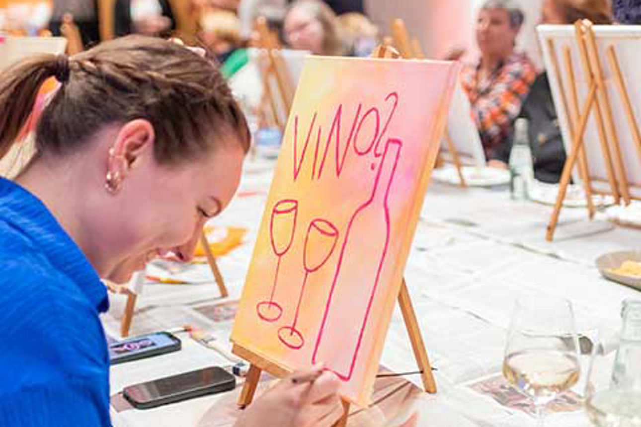  An einem langen Tisch sitzen Frauen mit ihren Staffeleien. 
