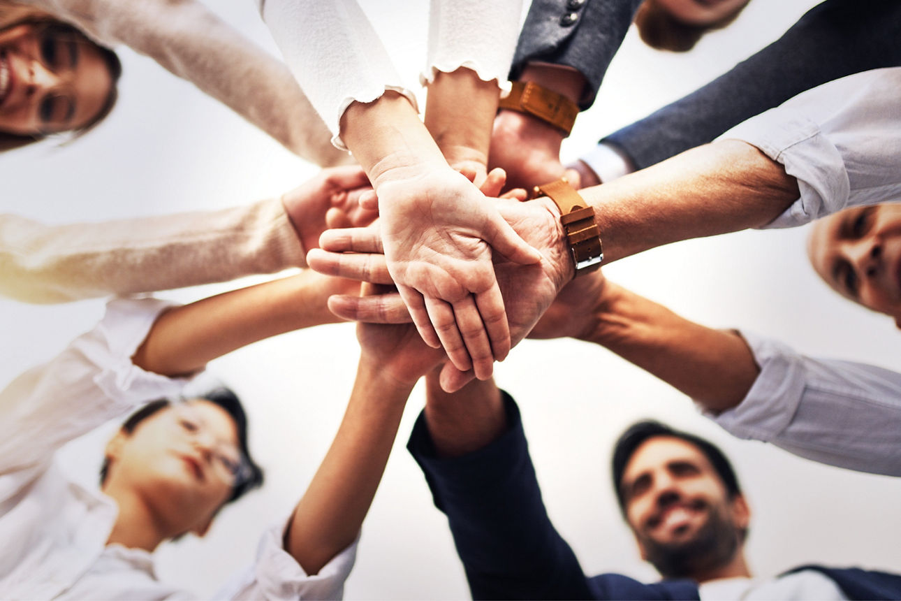 Eine Gruppe von 6 Personen stehen im Kreis und legen die Hände in der Mitte übereinander,.