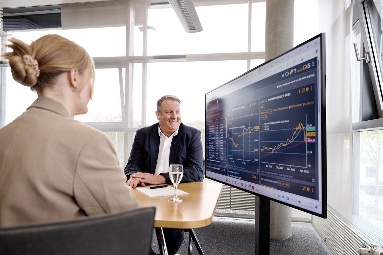Kundin mit Ihrem Berater vor einem großen Monitor mit einem Diagramm