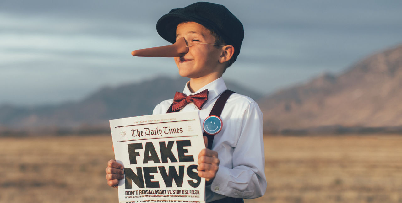 EIn kleiner Junge hat die Daily Times in der Hand, auf der groß "Fake News" steht und eine lange Nase aufgesetzt.