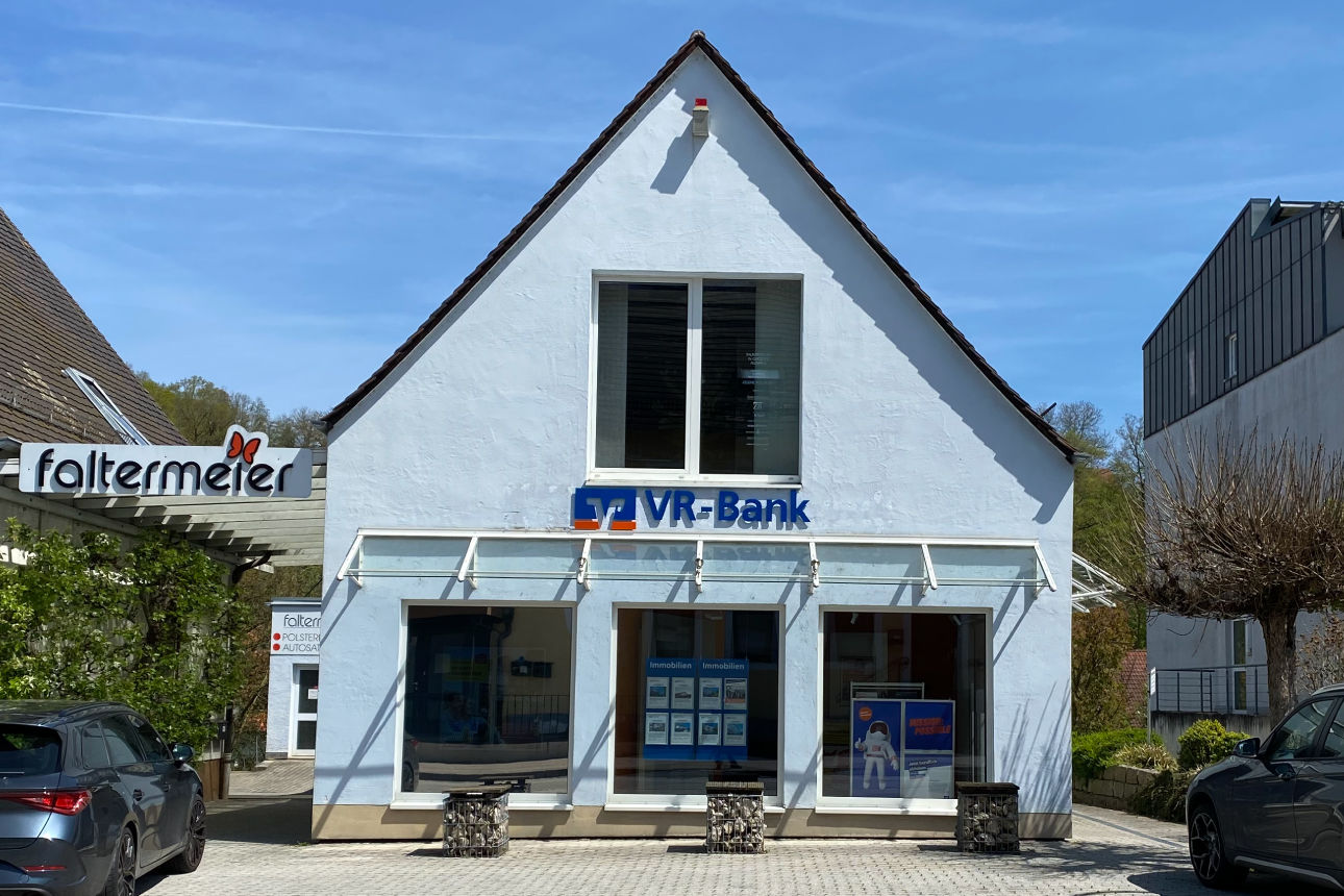 Ein kleines, spitzes, hellblaues Haus an einer Hauptstraße.