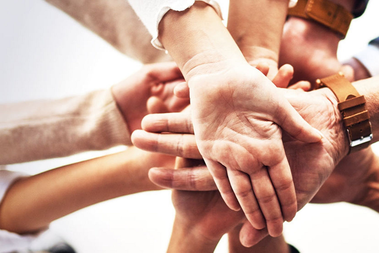 Mehrere Menschen eines Teams legen Hände übereinander