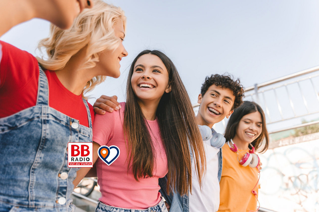 Vier junge Menschen lachen zusammen im Freien, freundliche Alltagsszene mit BBBank-Logo