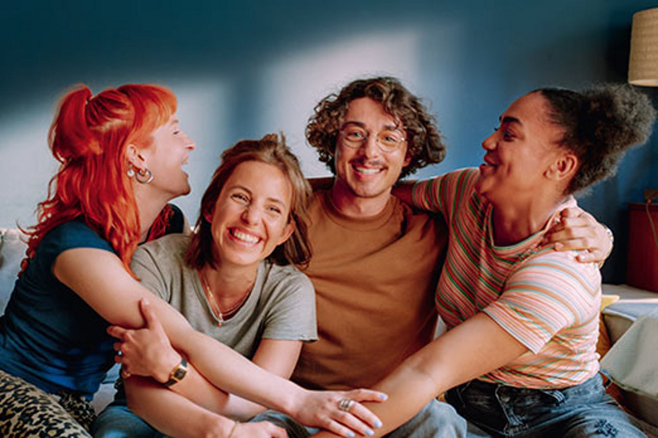 Drei Frauen und ein Mann sitzen gemeinsam auf dem Sofa und sind am lachen