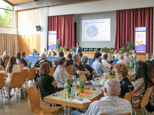 Viele Menschen nehmen an einer Hauptversammlung teil und beobachten einen Mann, der auf einer Bühne spricht