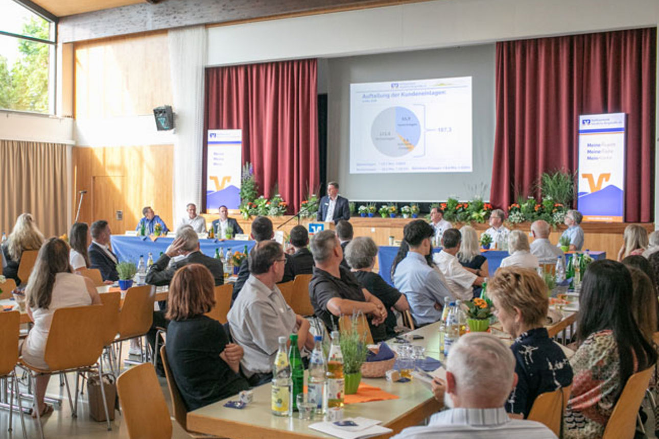 Viele Menschen nehmen an einer Hauptversammlung teil und beobachten einen Mann, der auf einer Bühne spricht