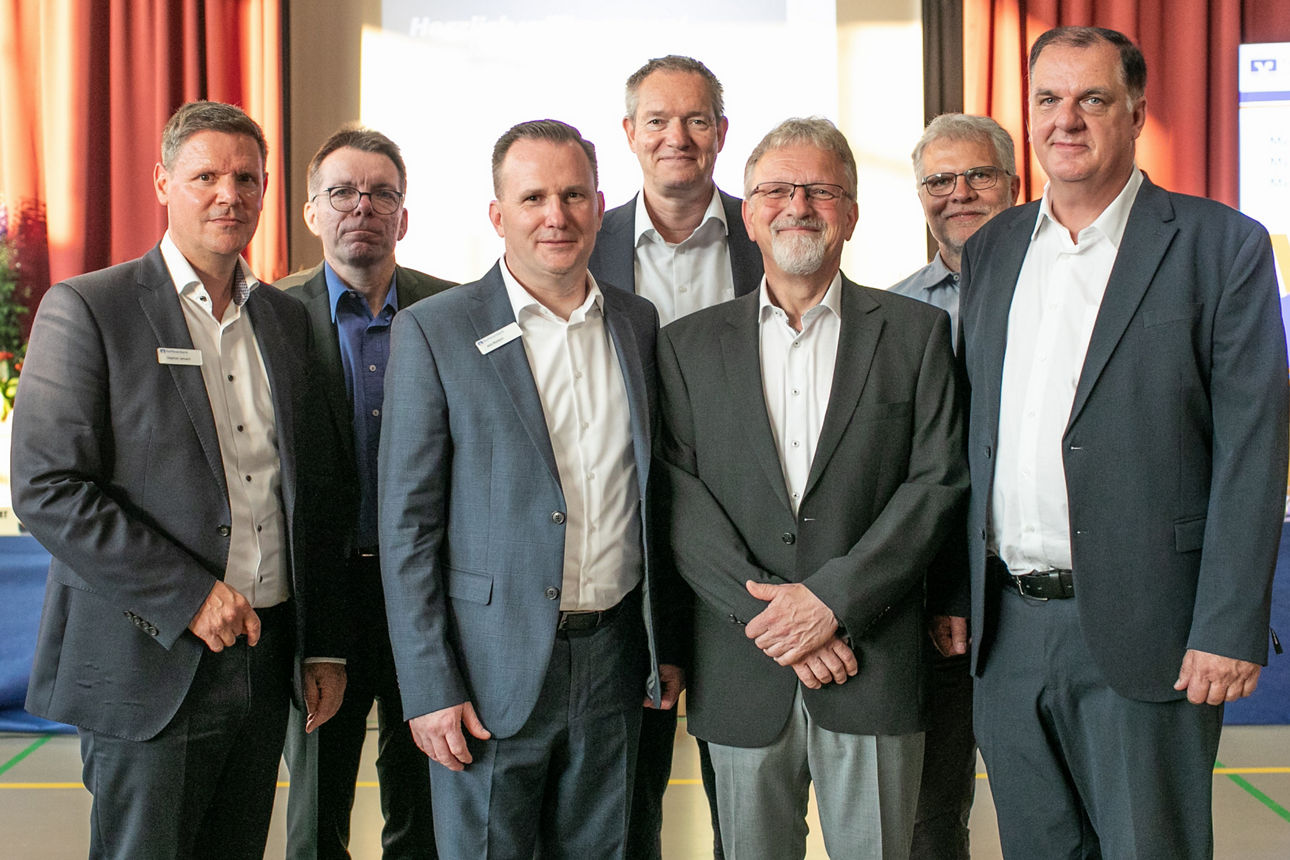 Sieben Männer in Anzügen blicken in die Kamera, die an der Generalversammlung teilnehmen