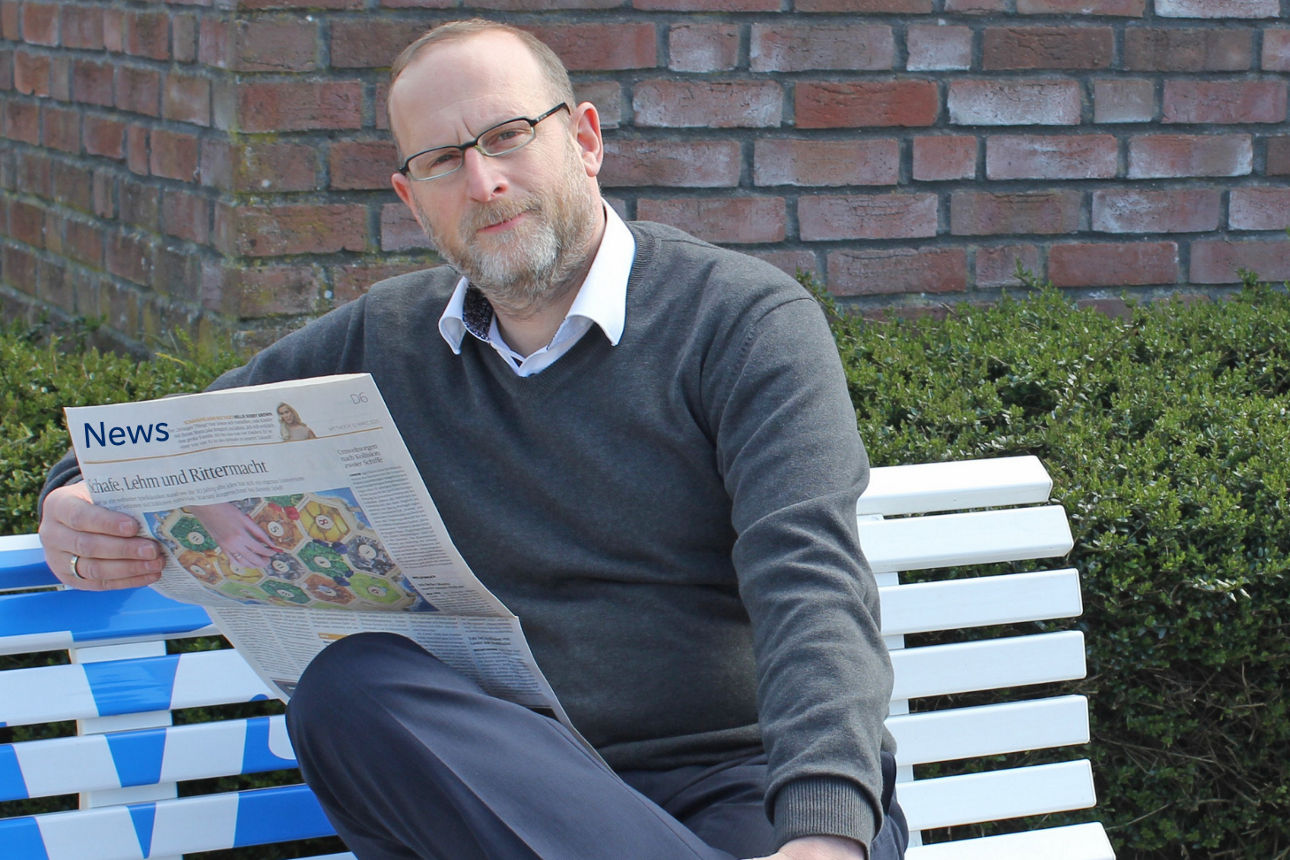 Junger Mann sitzt mit Zeitung auf einer Bank