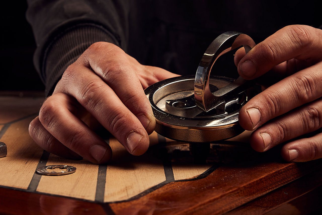 Hände justieren ein metallisches Präzisionsbauteil auf Holz – Sinnbild für Sorgfalt und Präzision im Wealth Management