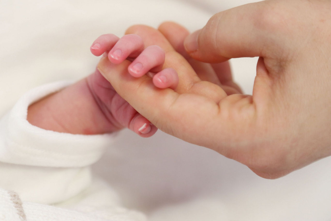 Eine Erwachsenenhand hält die Hand eines Neugeborenen