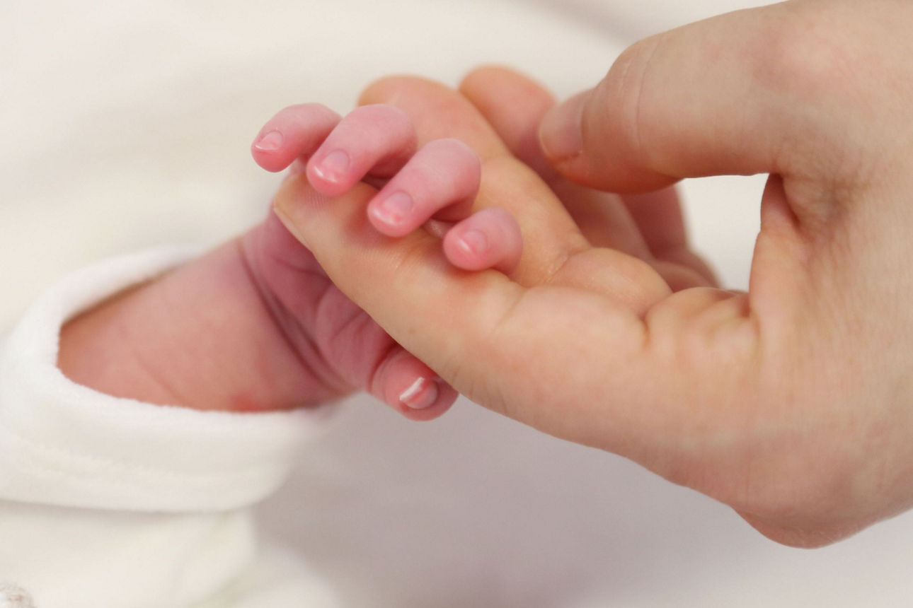 Eine Erwachsenenhand hält die Hand eines Neugeborenen