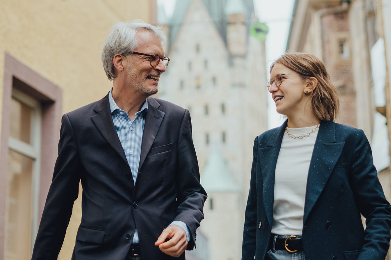 Zwei Mitarbeitende laufen vor dem Paderborner Dom entlang