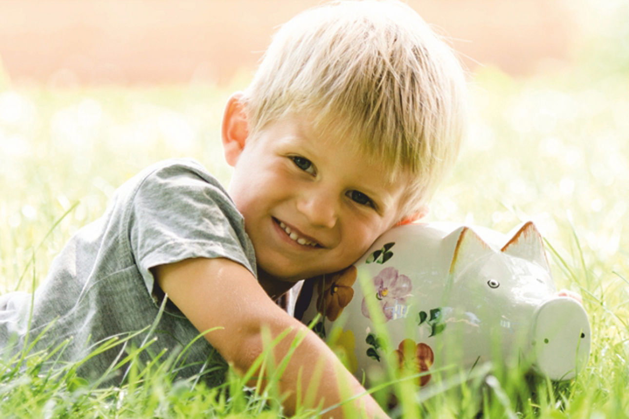 Kind liegt mit einem Sparschwein auf der Wiese
