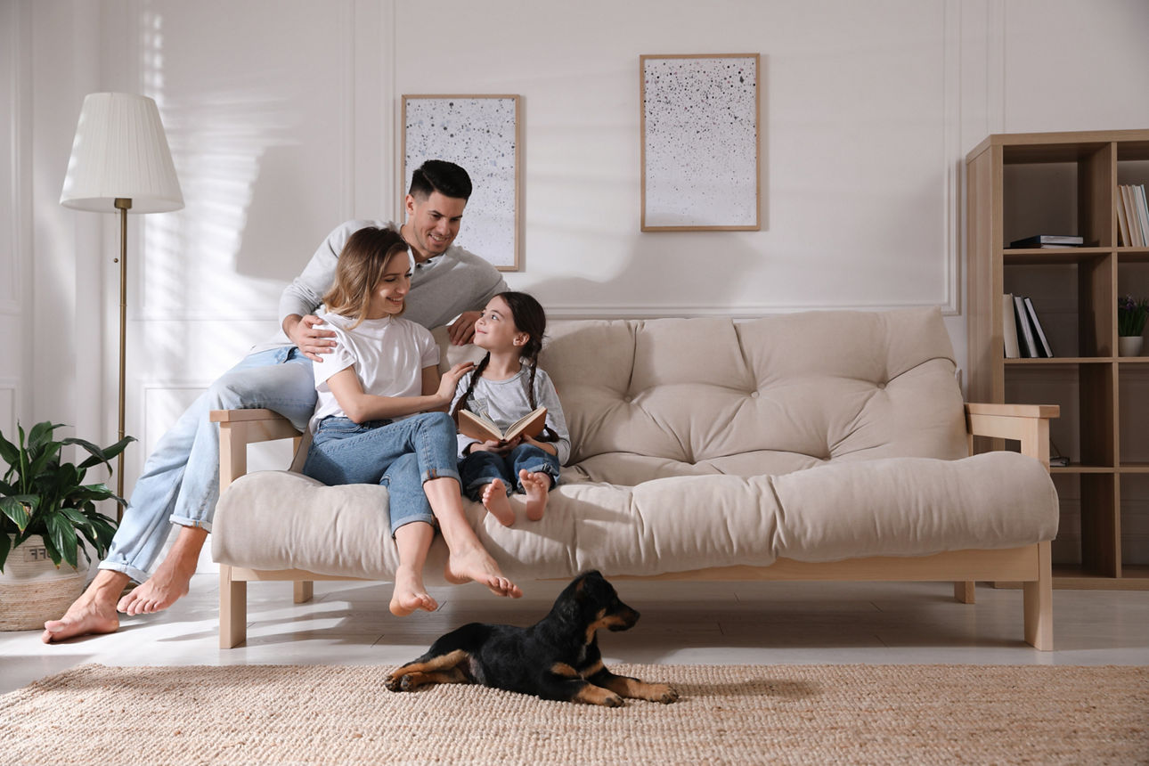 Eine junge Familie sitzt im Wohnzimmer auf dem Sofa und liest.
