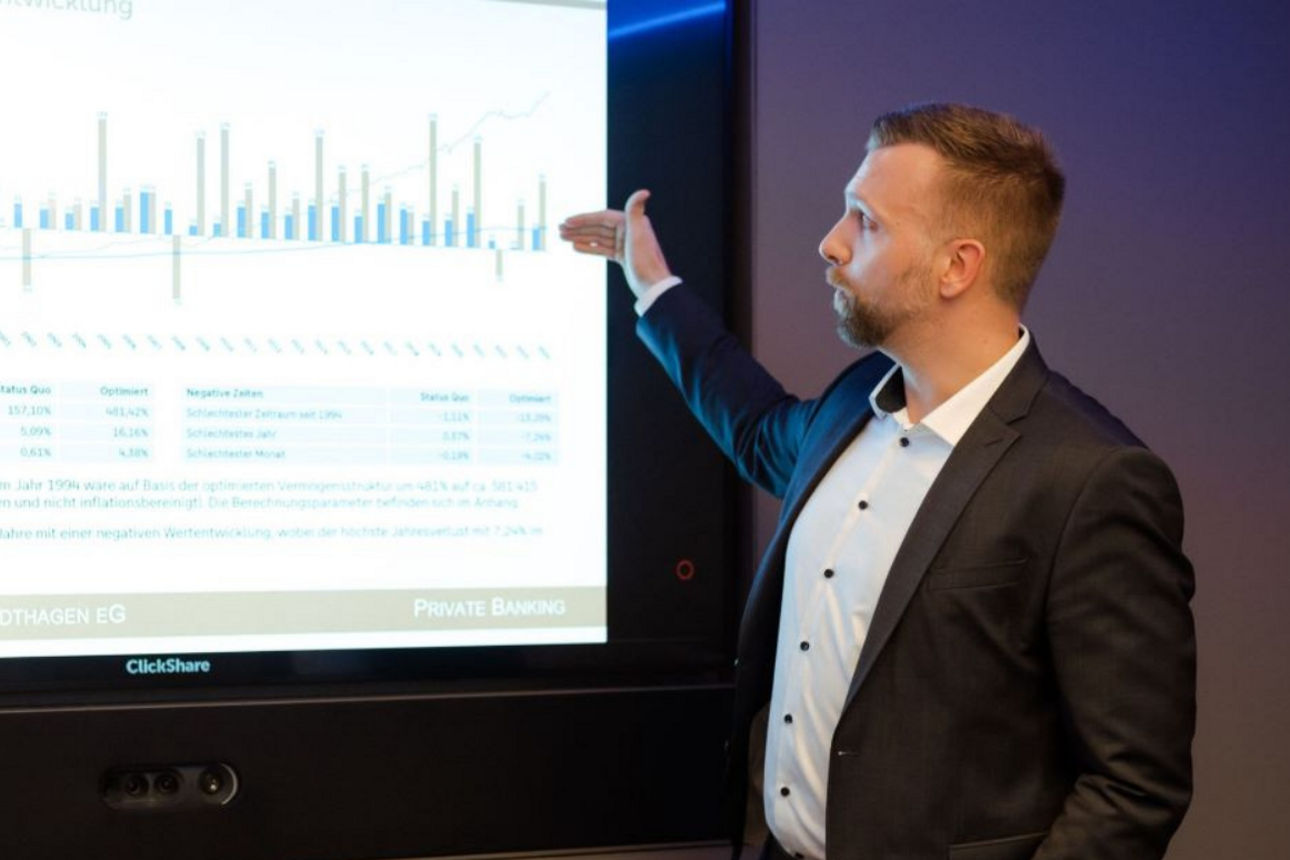 Ein Mann steht vor einem Bildschirm und zeigt auf einen Graph