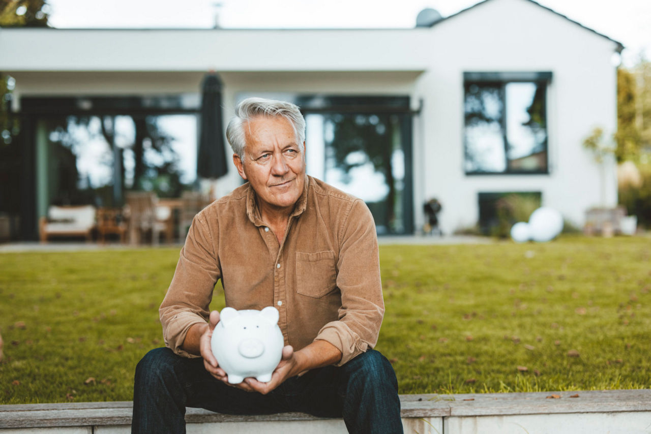Älterer Mann mit Sparschwein im Garten sitzend