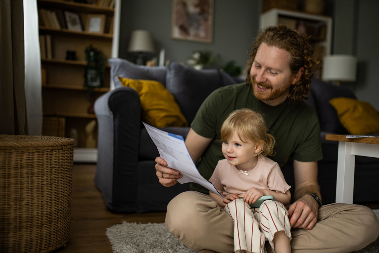 Glücklicher Vater, der mit seiner kleinen Tochter zu Hause Finanzrechnungen liest.
