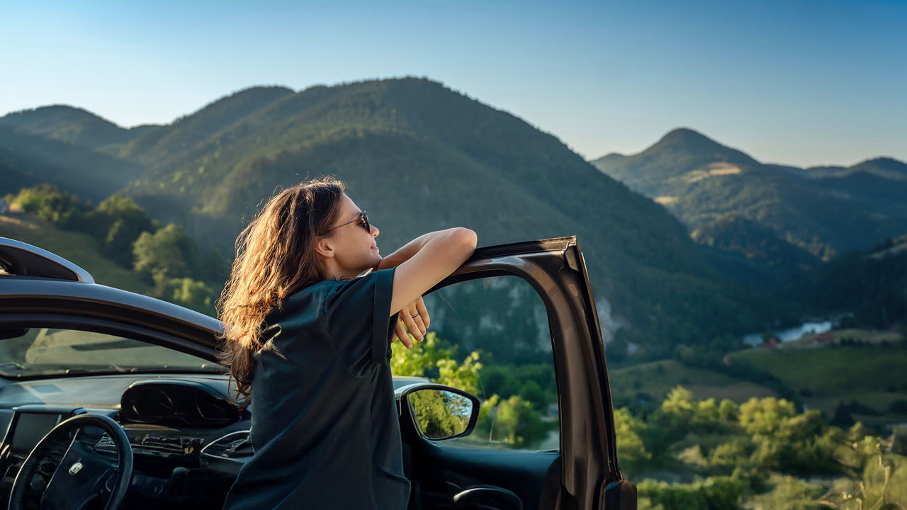 Junge Frau steht an Ihrem Auto und schaut in die Landschaft
