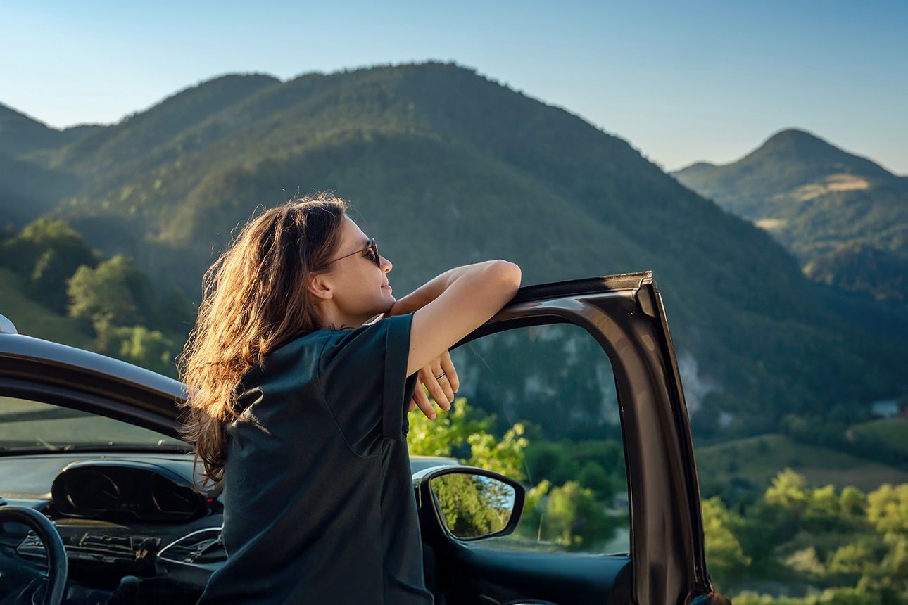 Junge Frau steht an Ihrem Auto und schaut in die Landschaft