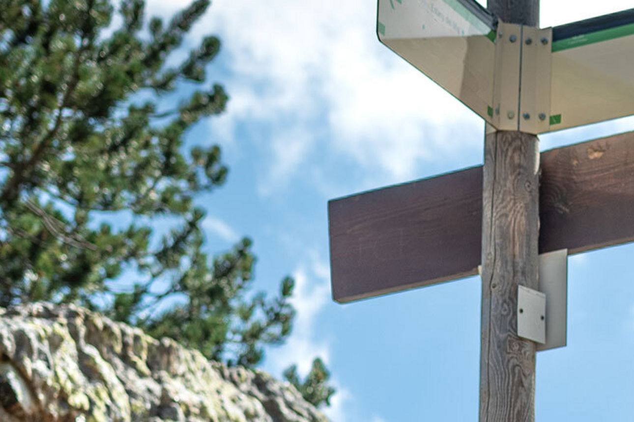 Wegweisschild in bergiger Landschaft auf das eine Frau schaut 